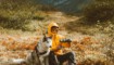 man met gele regenjas zit met zijn hond in de bergen iets te drinken